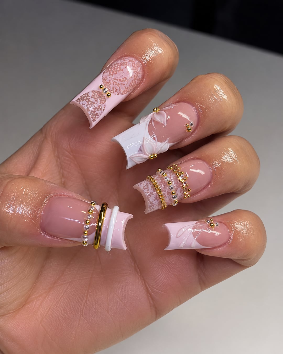 Ongles longs rose pâle avec dentelle, fleurs 3D, perles et anneaux dorés